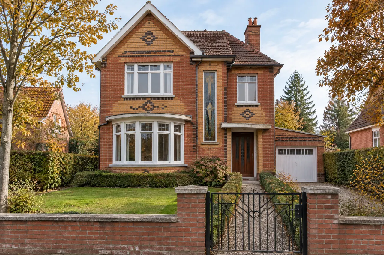 Villa des années 1930 en brique rouge et ocre à décors géométriques, bow-window arrondi, jardin devant et porte de garage