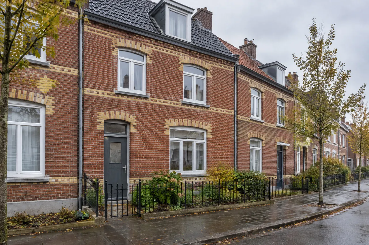 Maison des années 1920 en brique rouge à décors de brique claire au-dessus des fenêtres, porte gris anthracite, rue arborée