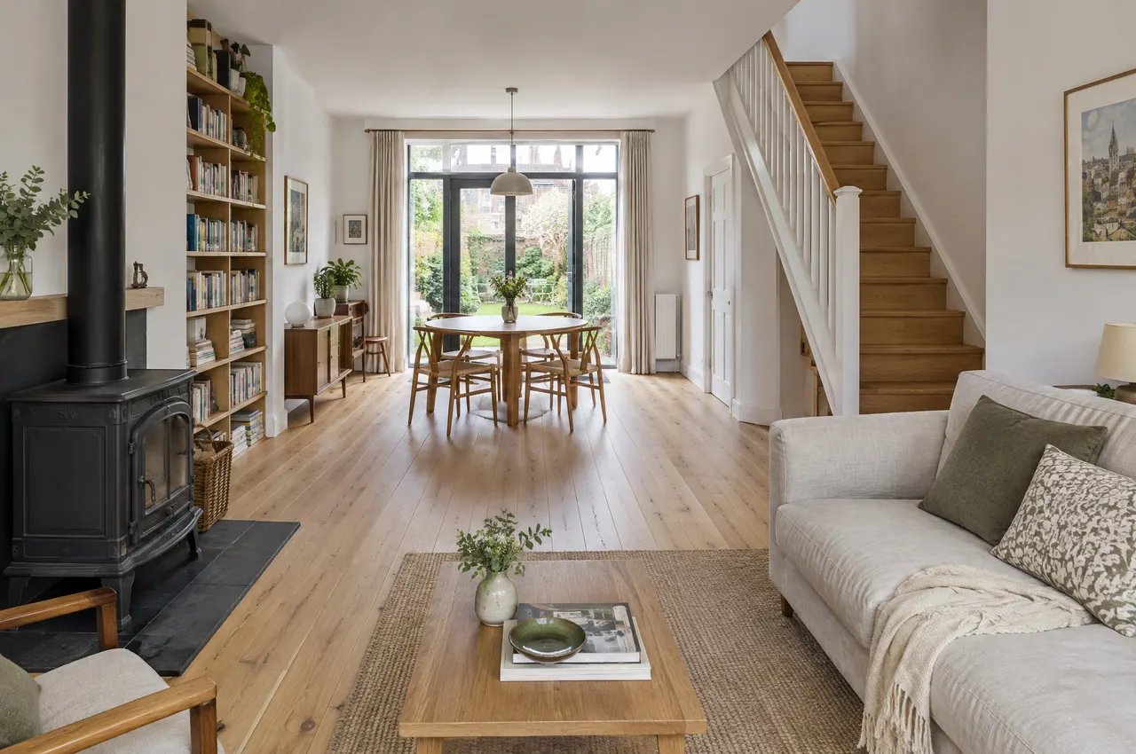 Séjour ouvert en chêne clair avec poêle à bois noir, escalier en bois et grande porte vitrée sur le jardin