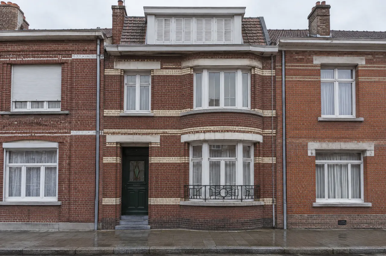 Façade de maison 1930 à Roubaix en brique rouge striée de briques vernissées crème, bow-window arrondi à garde-corps Art déco, porte vert foncé à vitrail